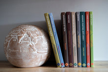 Load image into Gallery viewer, A row of Grassmarket Press books on a wooden surface next to a decorative sphere with engraved map.
